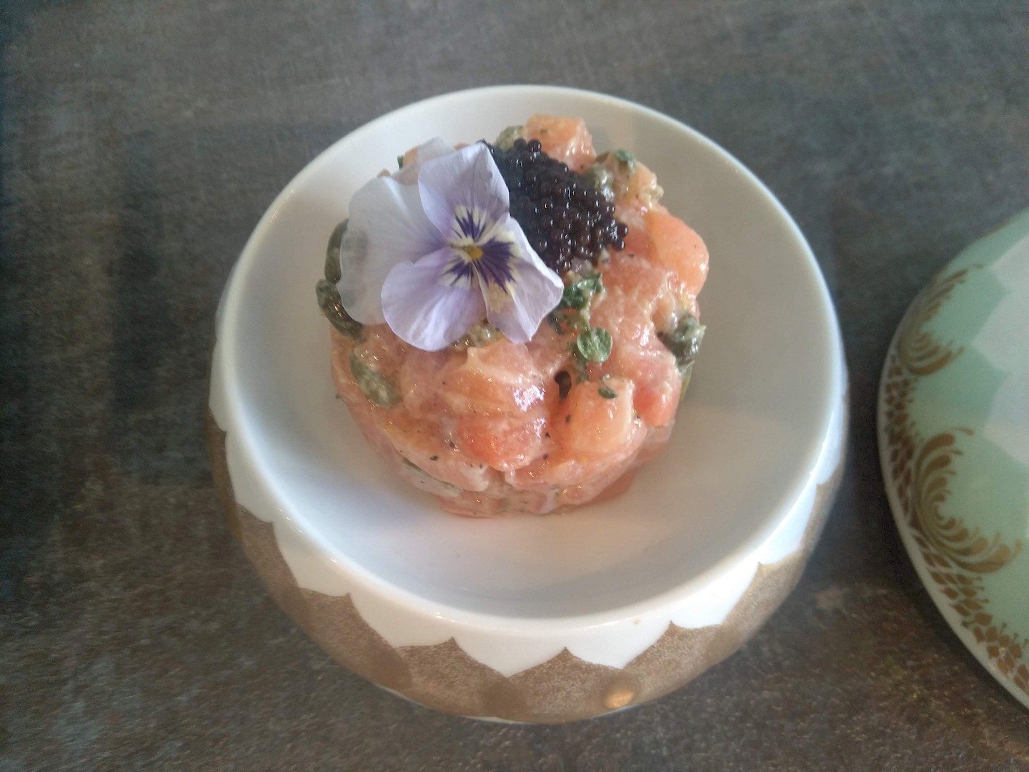 Ein Schälchen mit einem Türmchen Lachstartar dekoriert mit Kaviar und einer Veilchenblüte.