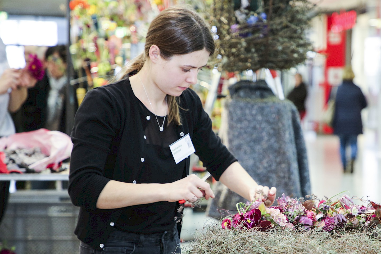 A young woman creates a floral arrangement on a wreath of twigs.