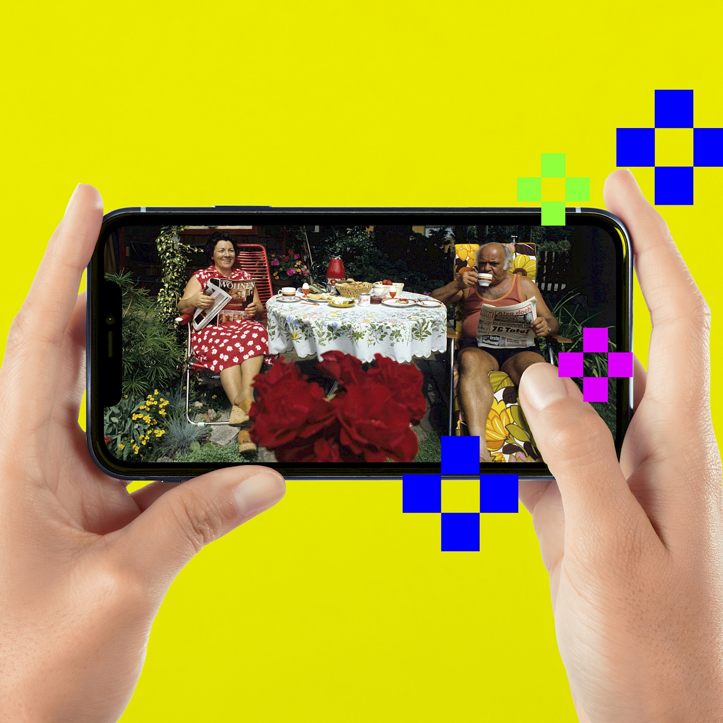 Eine Person hält ein Handy in der Hand. Darauf ist ein Foto zu sehen mit dem Titel „Schrebergartenidylle“. Ein Ehepaar sitzt in Liegestühlen an einem gedeckten Tisch in seinem Kleingarten.