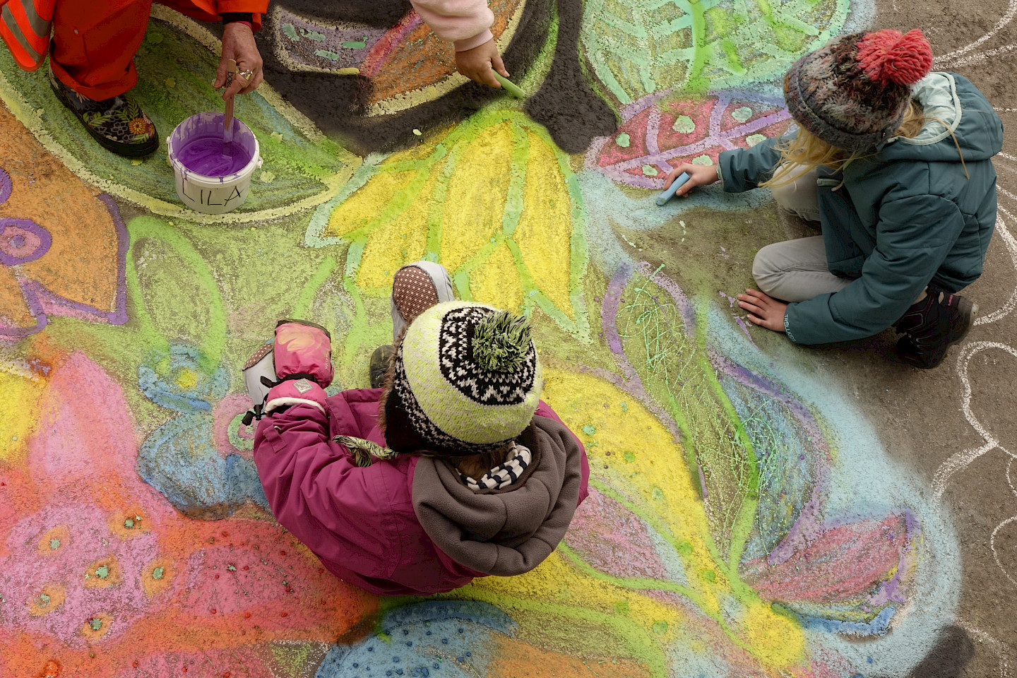 Kinder sitzen auf dem Boden und malen Blumenbilder mit Kreide.