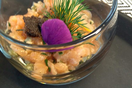 Ein kleines Glasschälchen mit Garnelenstücken dekoriert mit Kaviar, Dill und einer lila Blüte.