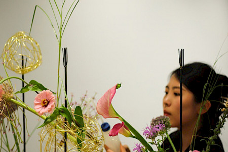 Eine Floristin arbeitet an einem Gesteck aus Blumen und Kugeln aus goldenen Metallfäden